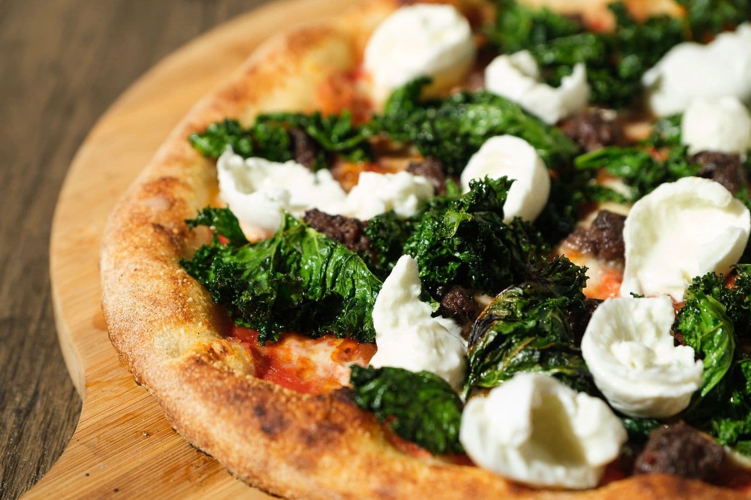 Round biga pizza with charred kale, sausage and ricotta.