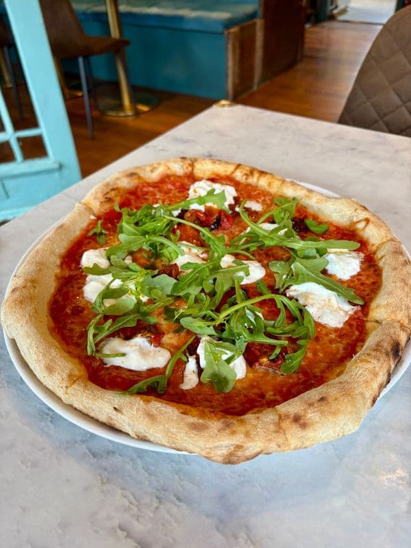 Round biga pizza topped with rocket, set against the teal banquette of Forager's Pizza & Pasta.