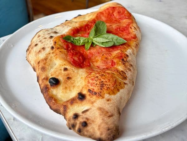 Folded calzone finished with fresh basil on a white plate.