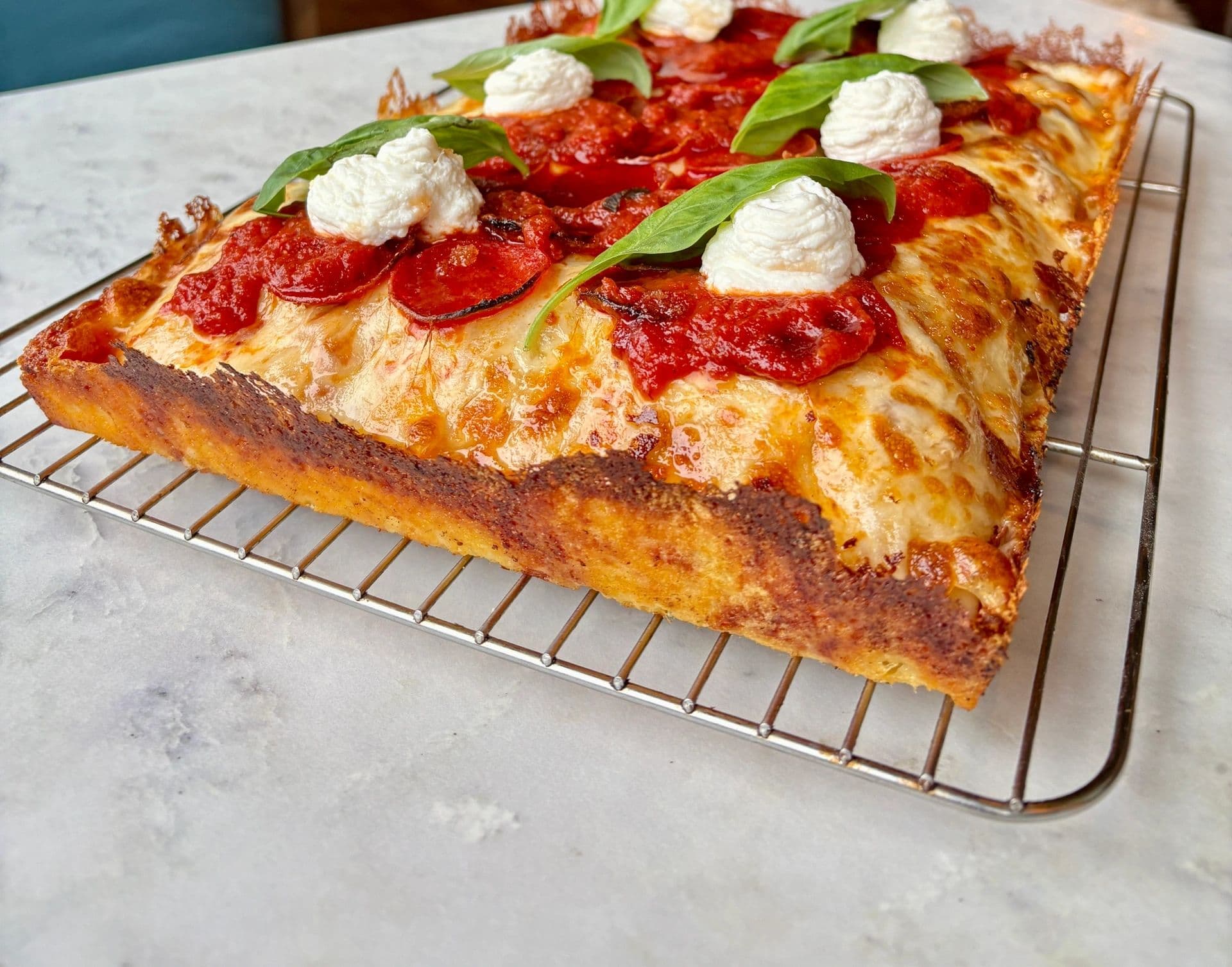 Detroit square pizza on a wire rack against the teal banquette and marble at Forager's Pizza & Pasta.